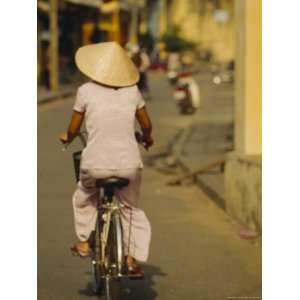  A Woman in a Conical Hat Rides Her Bicycle Down an Old Street 